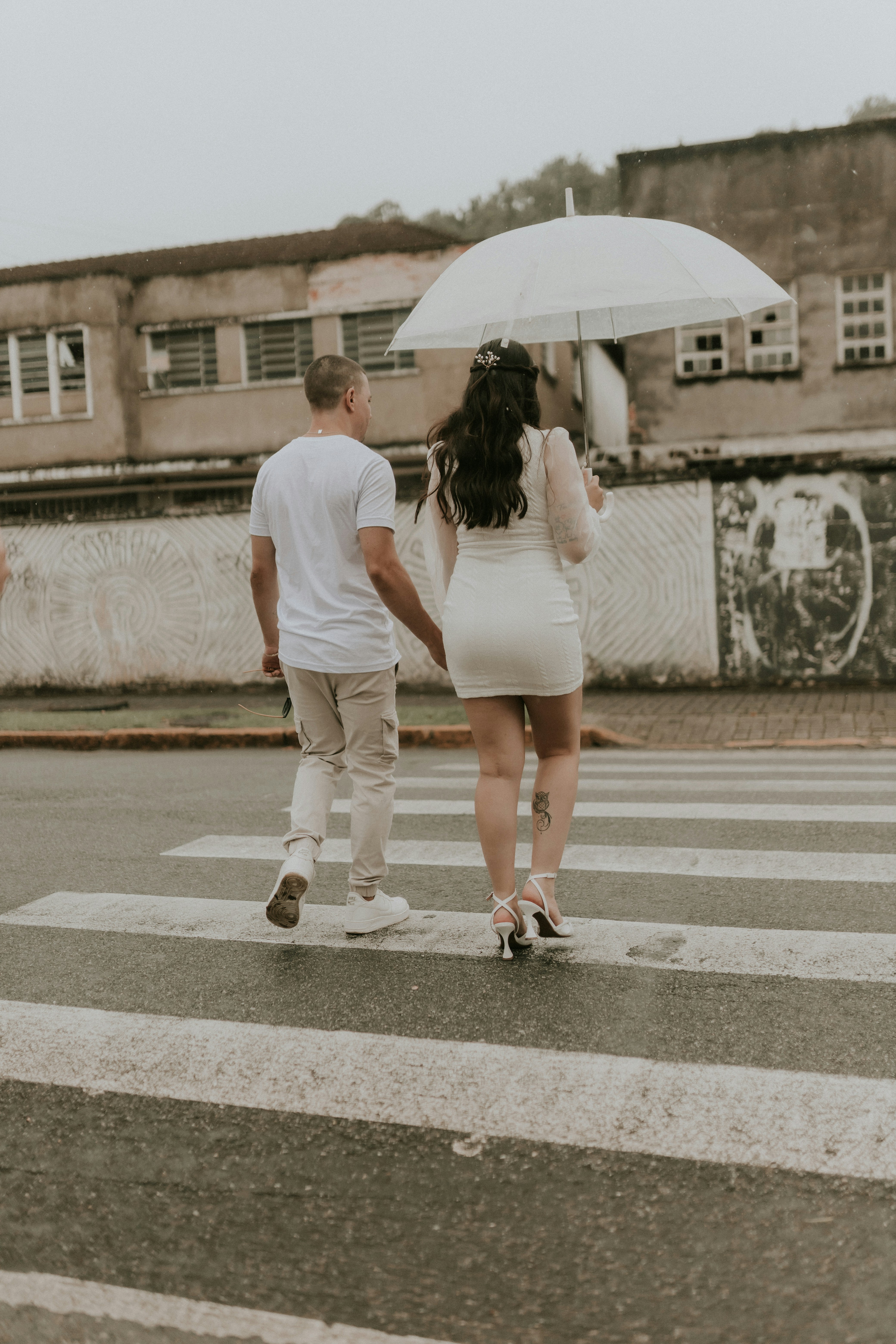 a man and a woman walking across a street holding an umbrella